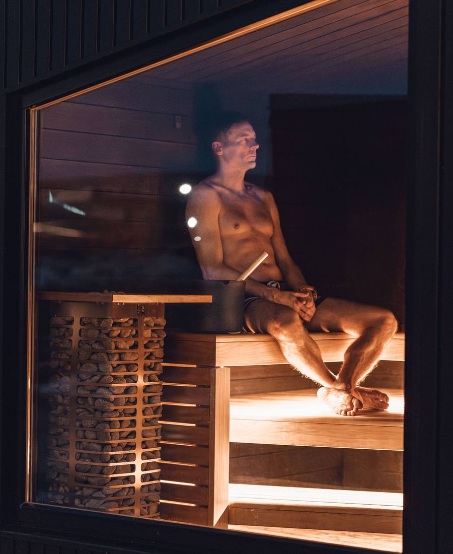 A person relaxing in an outdoor sauna at night, seen through a large window